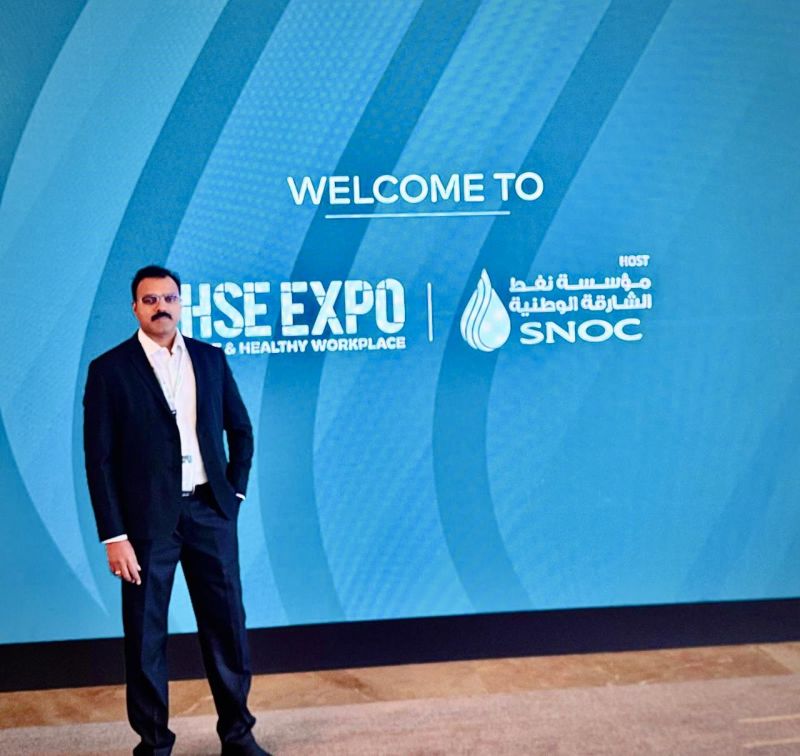 Team member standing in front of the HSE Expo SNOC welcome backdrop in Sharjah